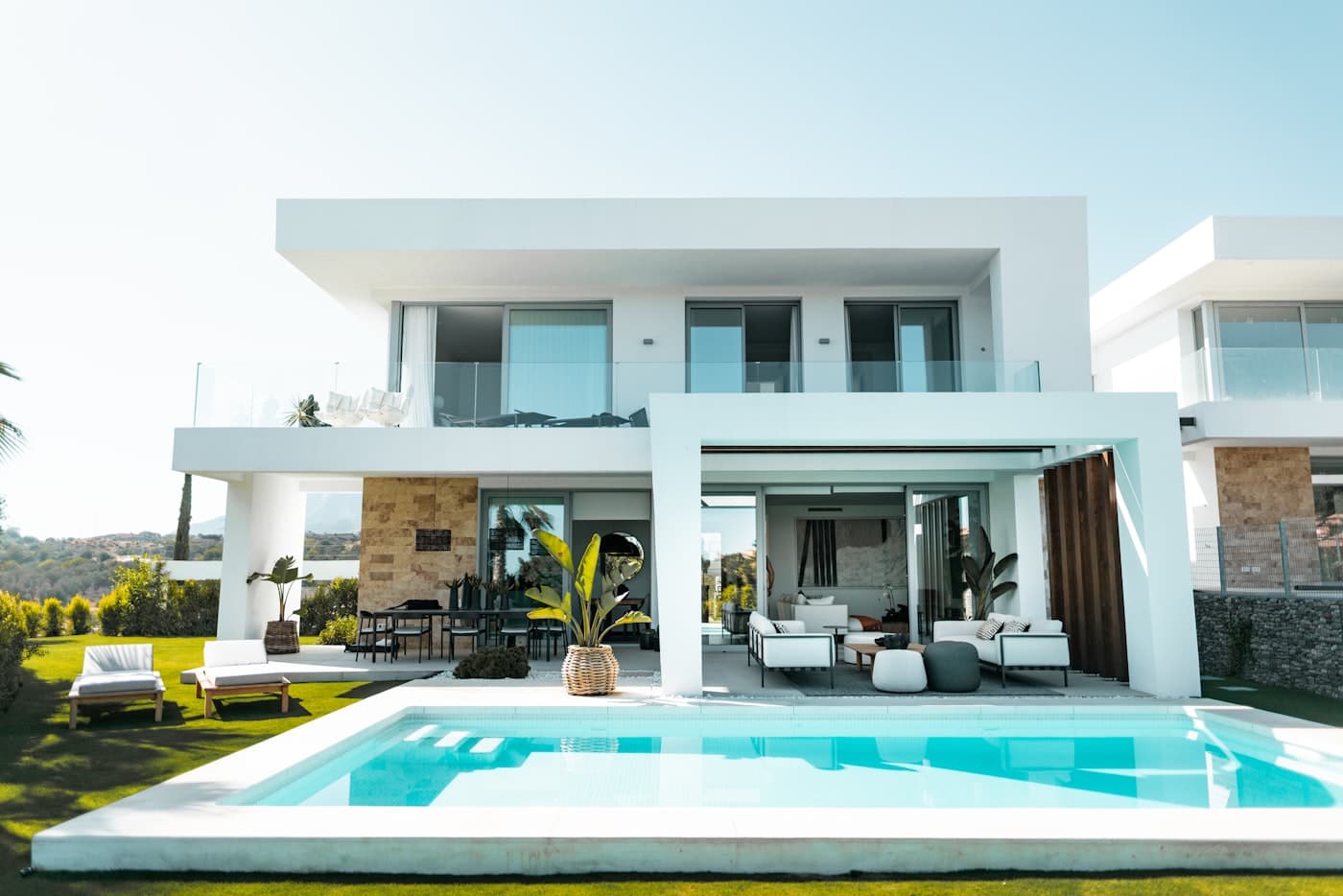 Bright white modern home with an outdoor lounge under a deep overhang, facing a large rectangular pool